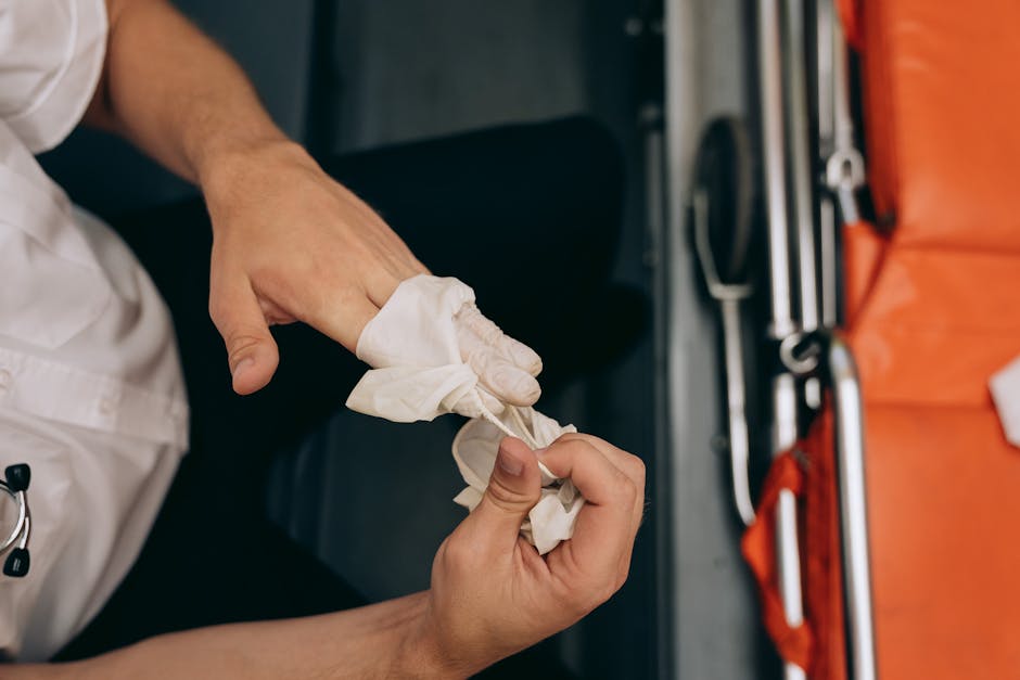 A close-up view of a person wearing a white work uniform wrapping a piece of white cloth or protective padding around their gloved hand, preparing for a furniture transport or packing process. The individual’s hands are central in the image, with one hand holding the cloth and the other adjusting or securing it. In the background, there are various tools and equipment typically used during house removals, including a portable step stool, metal bars, and straps, situated on an orange work surface or box. The setting appears to be inside a property or a van, with soft lighting highlighting the detailed actions involved in packing or preparing fragile items for a home relocation. This image exemplifies careful packing during the loading process coordinated by [COMPANY_NAME], which offers professional removals and furniture transport services, as indicated by the context of the house removal page for Selhurst residents.