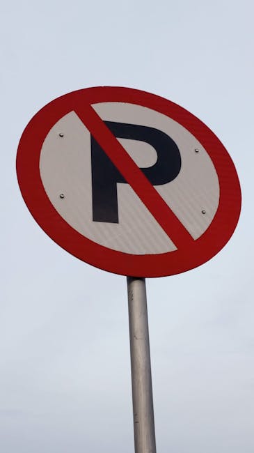 A yellow warning sign attached to a black metal pole indicating 'Parking suspension' beneath a larger informational sign, with a background of blurred trees and a fence. The sign is positioned on a pavement near a property, suggesting restrictions relevant to house removals and moving logistics. The area is well-lit, highlighting the text and the sign's visibility for passing vehicles and pedestrians involved in furniture transport or home relocation activities. The scene reflects the typical signage encountered during organised removals, where parking restrictions facilitate the loading and unloading process for vehicles such as vans or trucks used by Man with Van Selhurst when assisting with house moves, packing, and furniture transport.